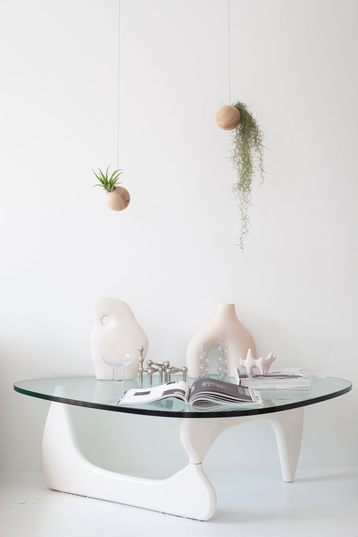 Modern glass coffee table with white legs against a white wall, featuring decorative vases and books.