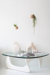 Modern glass coffee table with white legs against a white wall, featuring decorative vases and books.