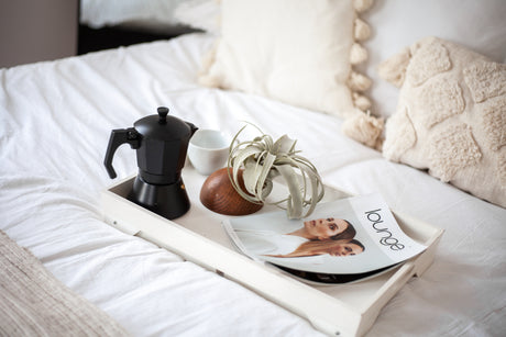 Tray with a coffee maker, plant, and magazine on a bed